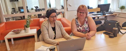 handledare inom Rusta och matcha handleder en deltagare. De sitter vid ett bord i ett stort rum och tittar tillsammans på datorn.